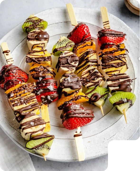 Plate of colorful fruit skewers with strawberries, kiwi, banana, and chocolate drizzle