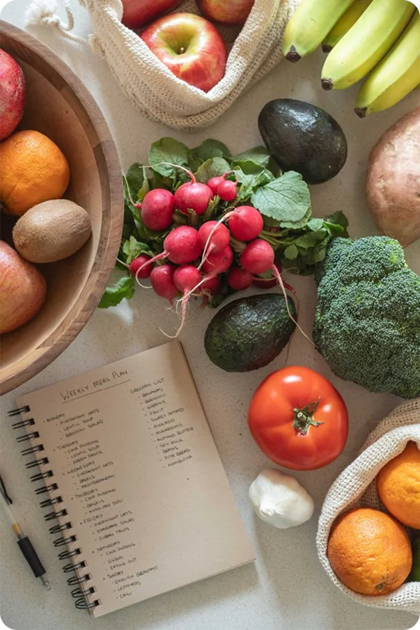 Fresh fruits, vegetables, and a weekly meal plan notebook on a counter